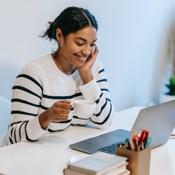 Smiling woman looking at computer with a cup of tea